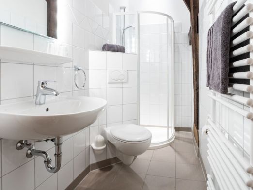 Modern eingerichtetes Badezimmer mit Waschbecken, Toilette, Dusche und Heizung, um die Handtücher zu trocknen